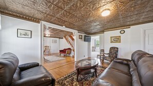 A living room with leather sofas, a glass coffee table, patterned rug, and a decorative ceiling. - Historic Sugar Loaf Farmhouse | 5BR | Sleeps 8 (Chester)