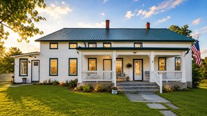 A two-story white house with a green roof, a front porch, and an American flag. - Historic Sugar Loaf Farmhouse | 5BR | Sleeps 8 (Chester)