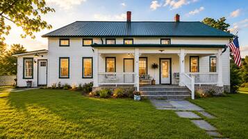 A two-story white house with a green roof, a front porch, and an American flag.