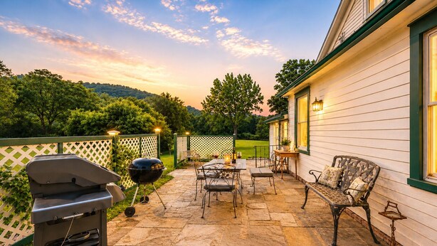 A patio with stone flooring, a grill, outdoor furniture, and a house with white siding and green trim. - Historic Sugar Loaf Farmhouse | 5BR | Sleeps 8 (Chester)