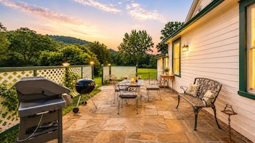 A patio with stone flooring, a grill, outdoor furniture, and a house with white siding and green trim.