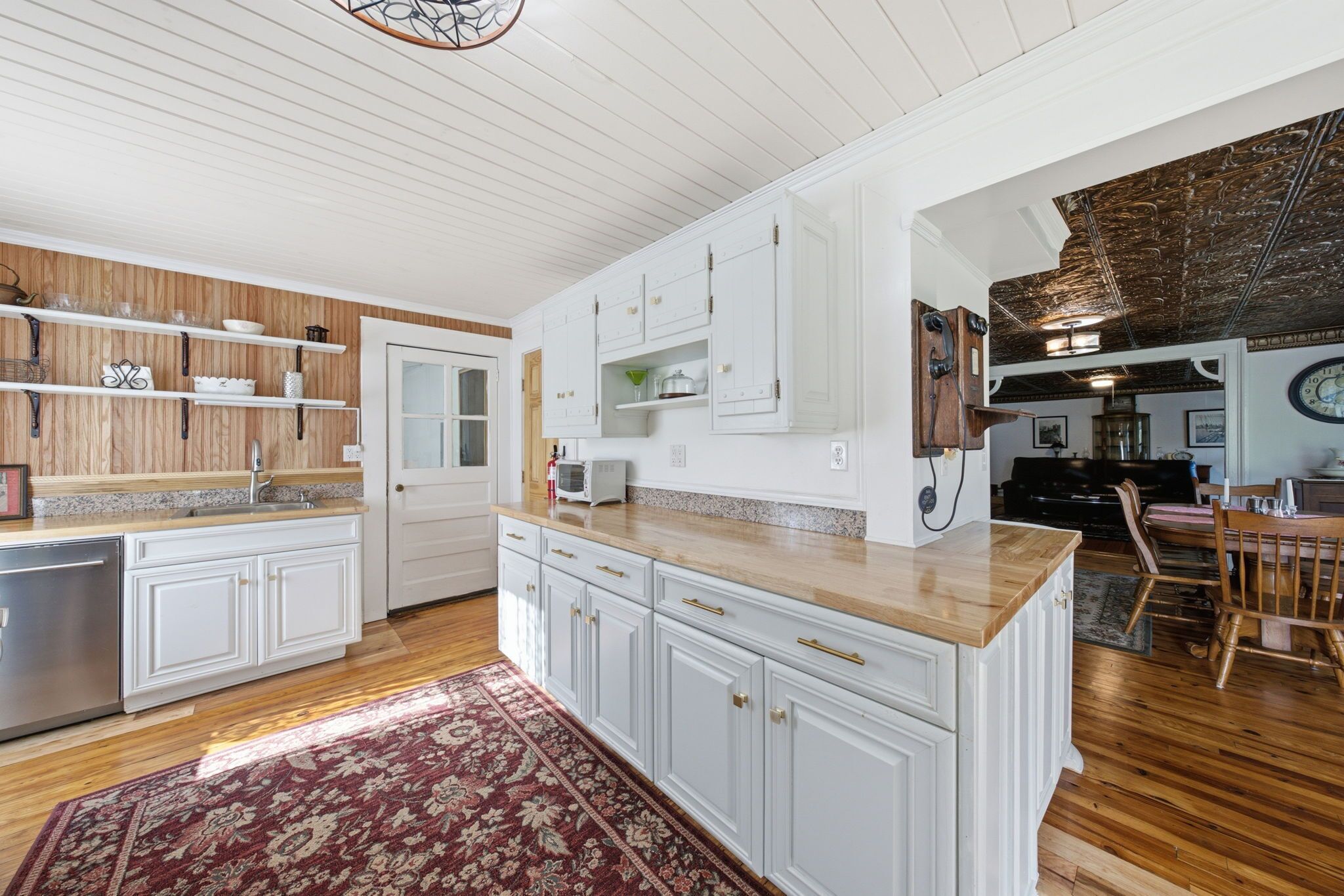 Une cuisine spacieuse avec des meubles blancs, un plan de travail en bois et un tapis rouge à motifs.