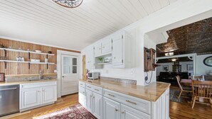 A spacious kitchen with white cabinetry, a wooden countertop, and a red patterned rug. - Historic Sugar Loaf Farmhouse | 5BR | Sleeps 8 (Chester)