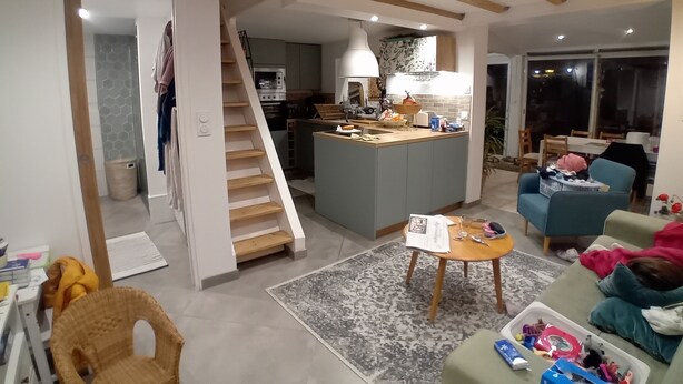 Ett modernt kök med en central köksö, en matplats med en soffa och en trappa som leder till ett annat våningsplan.