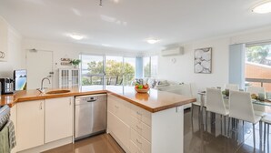 Une cuisine moderne avec un plan de travail en bois, des meubles blancs, un lave-vaisselle et un coin repas comprenant une table en verre et des chaises blanches.