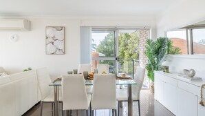 Une cuisine moderne avec un coin repas, des meubles blancs et une vue sur l’extérieur.