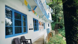 A building with blue-framed windows, a covered outdoor seating area, and a staircase leading to a garden.