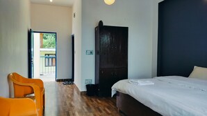 A hotel room with a bed, wooden flooring, a wardrobe, a chair, and a door leading to an outdoor area.