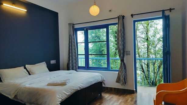 A bedroom with a bed, a window with curtains, a hanging light fixture, and a view of greenery outside.