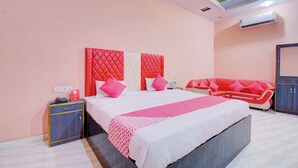 A hotel room with a bed, a nightstand, a red sofa, and an air conditioning unit.