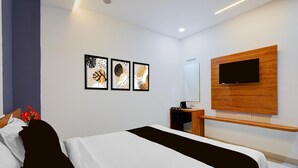 Ett modernt hotellrum med en säng, ett skrivbord, en stol, en tv som är monterad på en träpanel och tre inramade konstverk på väggen.