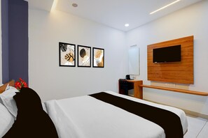 Ein modernes Hotelzimmer mit einem Bett, einem Schreibtisch, einem Sessel, einem an einer Holzvertäfelung montierten Fernseher und drei gerahmten Kunstwerken an der Wand.
