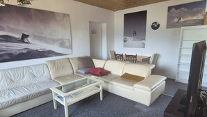 A living room with a sofa, a glass coffee table, a TV, and wall art.