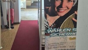 A hallway with a red carpet, a poster on the wall, and a door leading to another room.