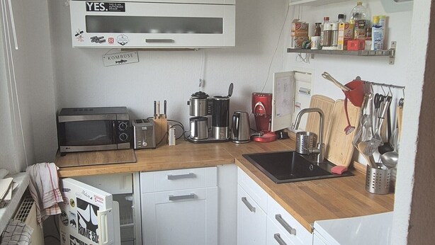 A compact kitchen with white appliances, a wooden countertop, and a ceiling fan.