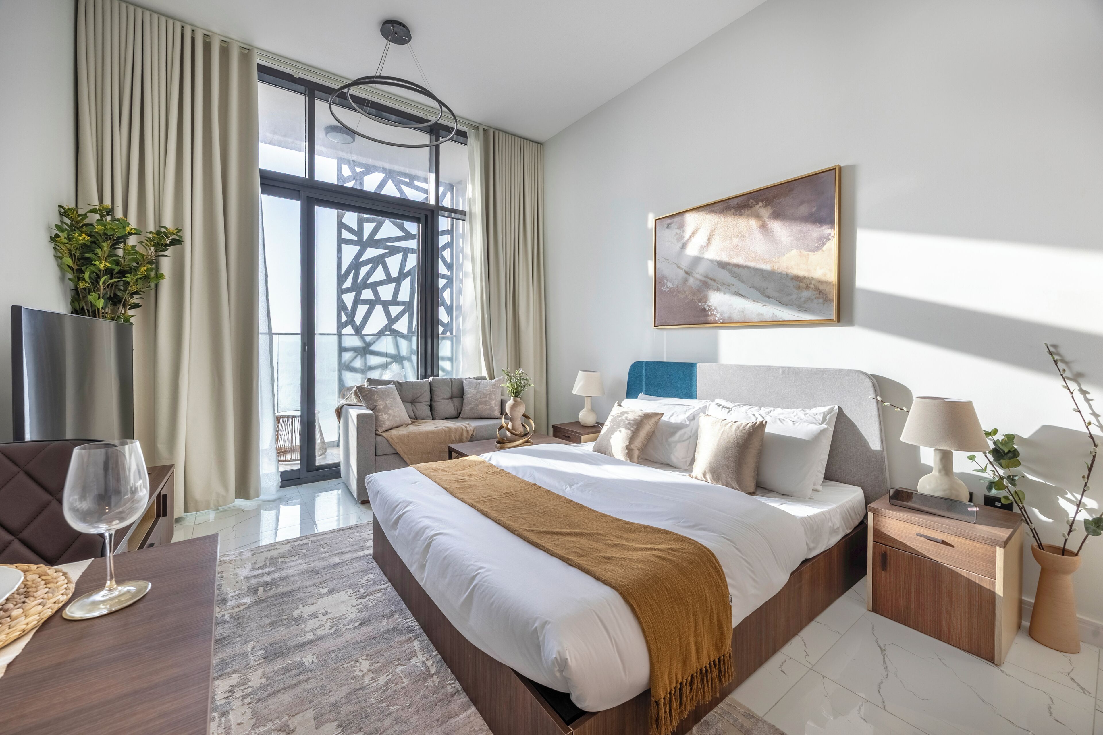 A modern hotel room with a large bed, bedside tables, a TV, and a view of the outdoors.