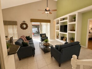A living room with two sofas, a coffee table, a TV on a shelf, and a ceiling fan.
