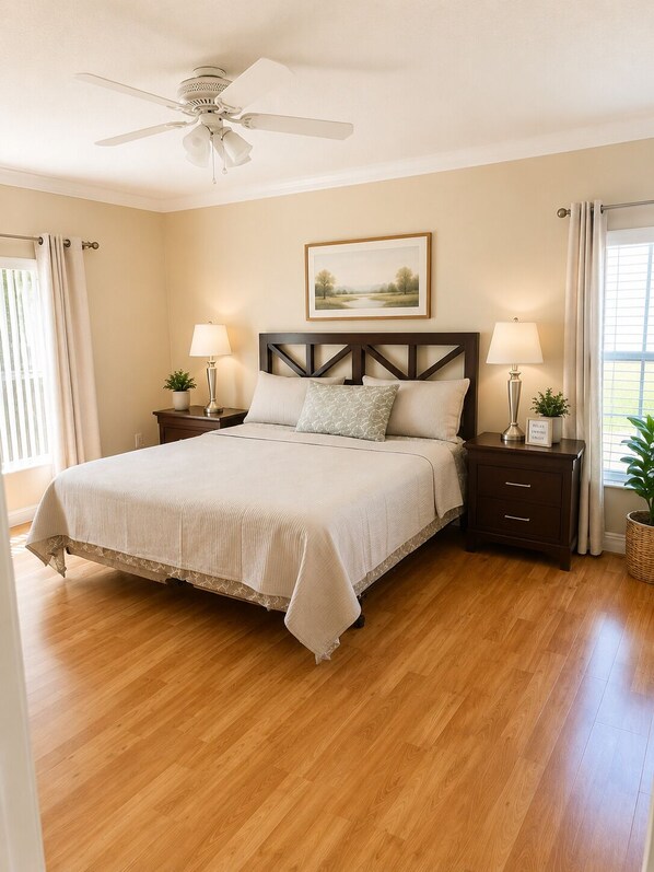 A bedroom with a bed, nightstands, a ceiling fan, a painting, and a window with curtains.