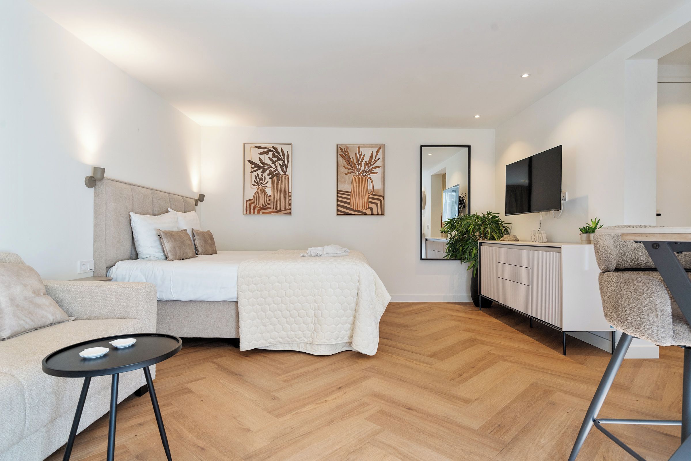 Un dormitorio moderno con cama, sofá, mesita y televisor.