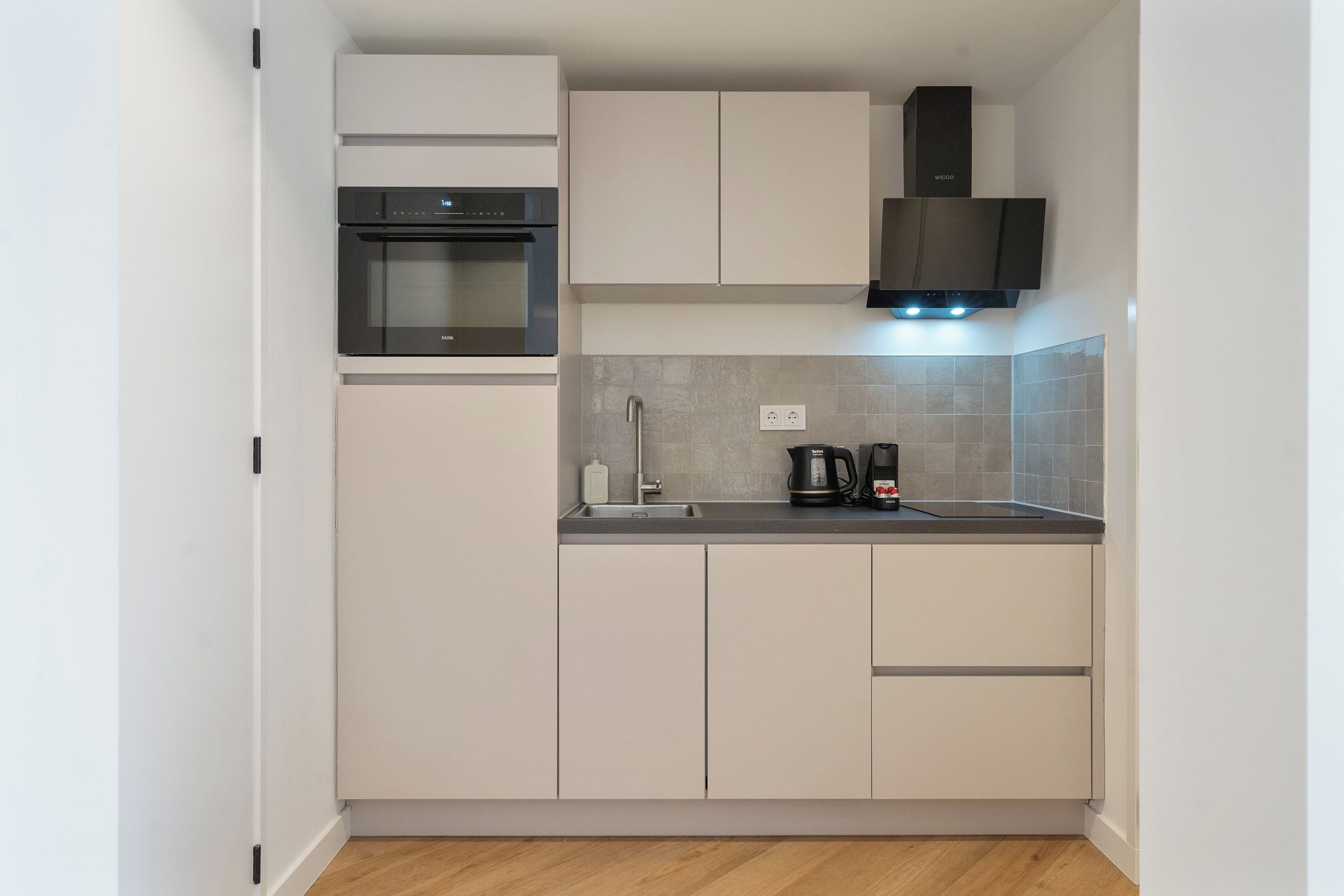 Una cocina moderna con armarios blancos, horno empotrado, cafetera y salpicadero de azulejos.