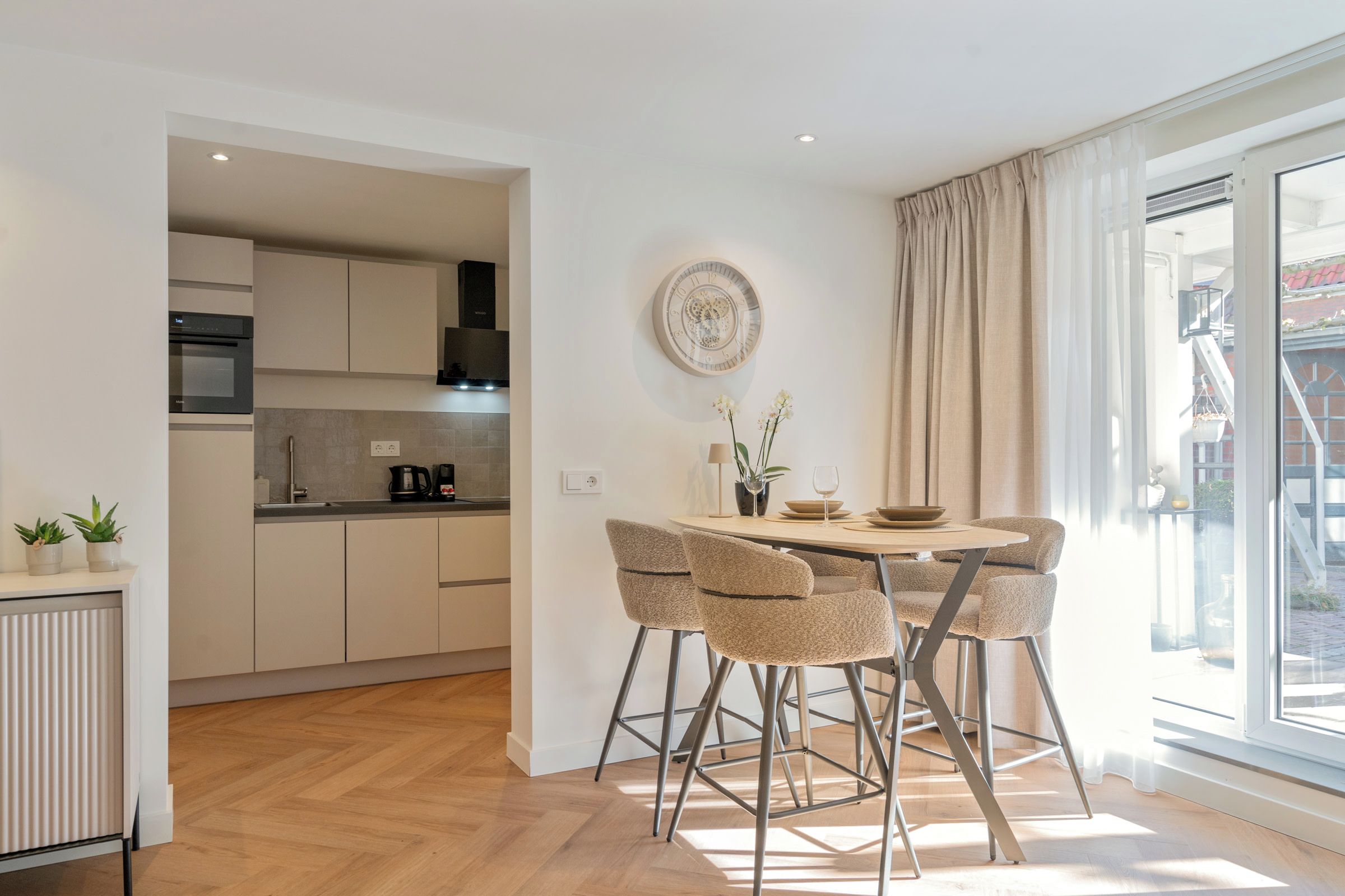 Una cocina moderna con armarios blancos, horno integrado y un comedor con una mesa redonda y cuatro sillas.