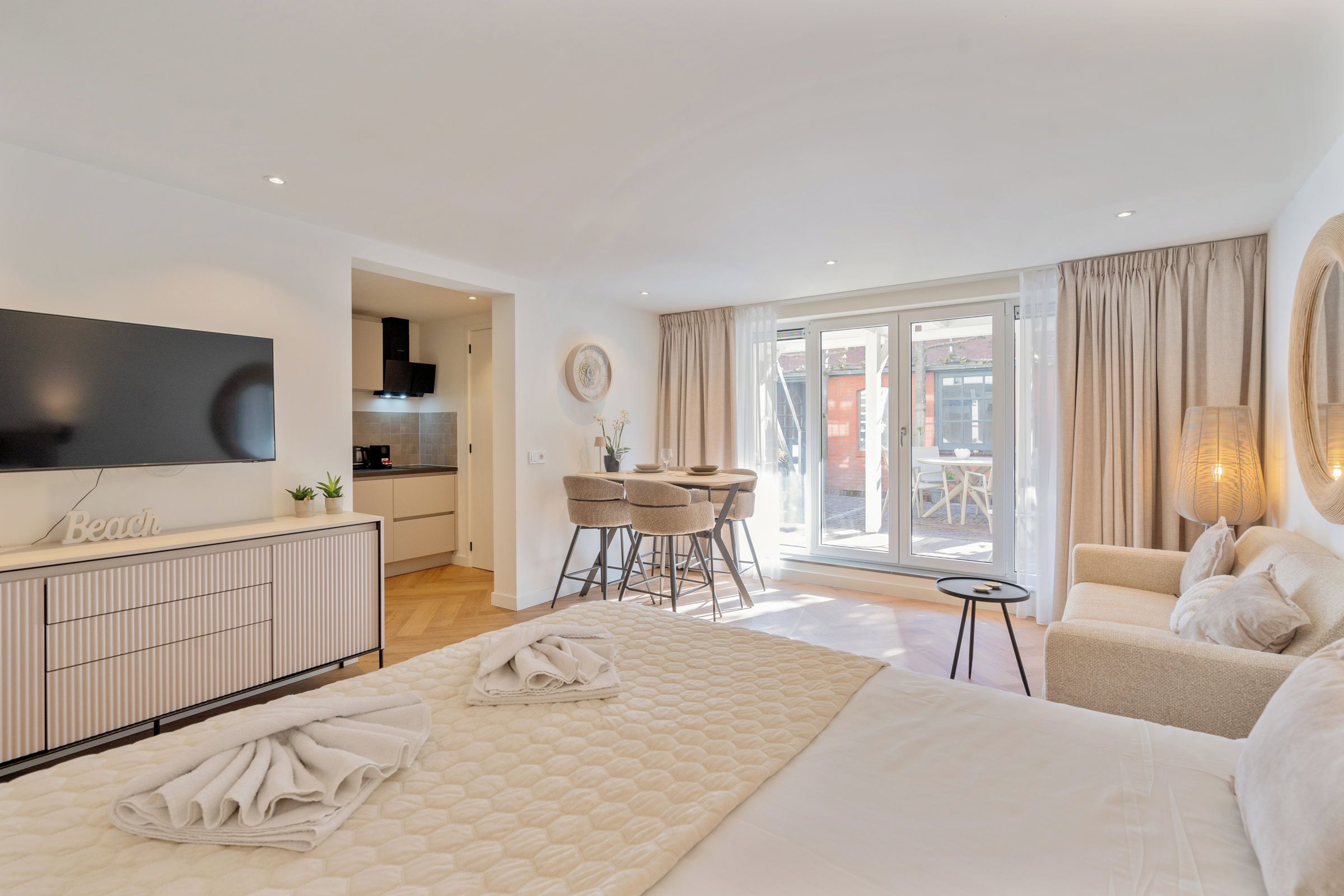 Habitación de hotel moderna con cama, televisor, zona de comedor y vistas al exterior.
