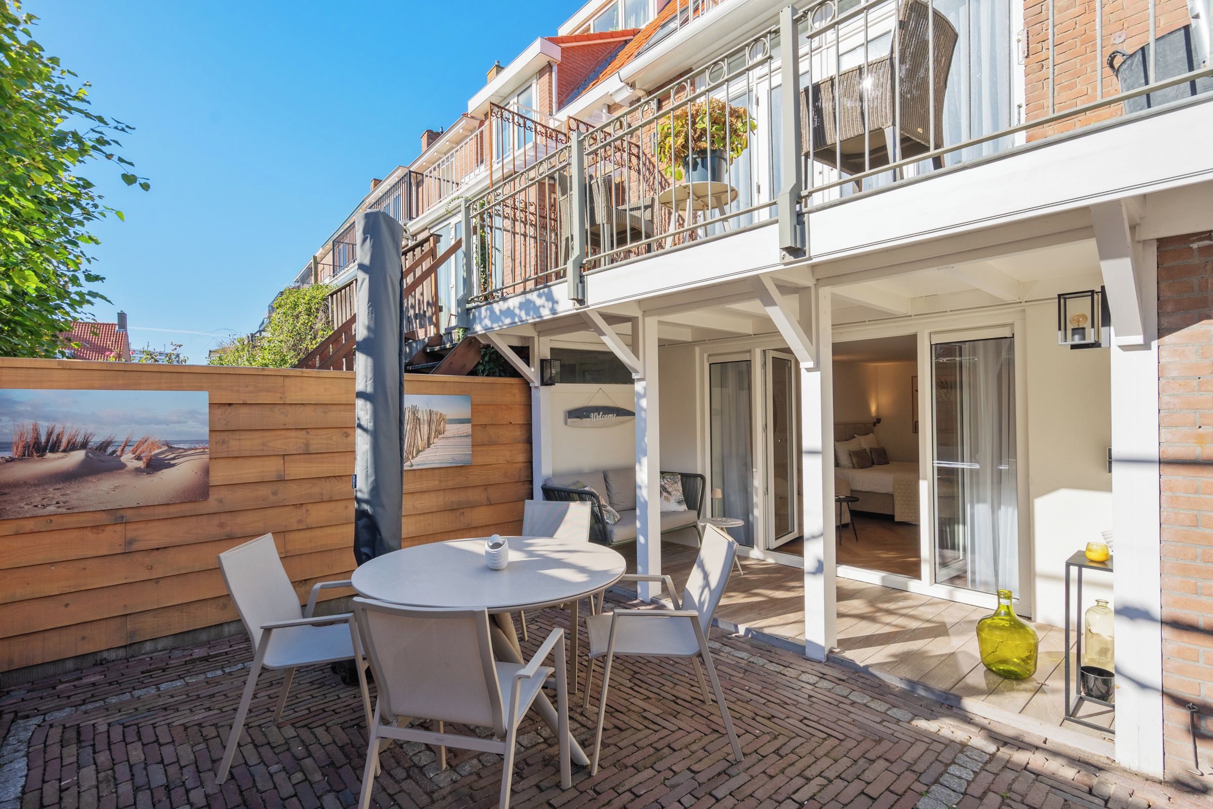 Un edificio de dos pisos con balcón, una terraza de madera y un patio con mesa y sillas.