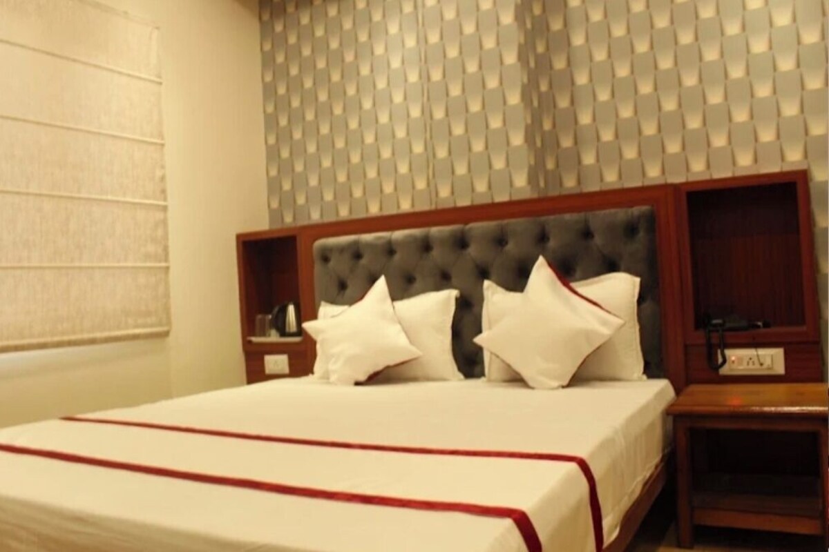 A hotel room with a large bed, a wooden headboard, a nightstand, and a wall with a textured pattern.