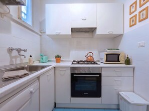 A compact kitchen with white cabinets, a Bosch oven, a gas stove, a vintage microwave, and a small sink. - Loft del Cefalo - In the heart of the old town (Roma)