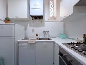 A compact kitchen with a built-in dishwasher, a stove, a sink, and a window with a lattice design. - Loft del Cefalo - In the heart of the old town (Roma)