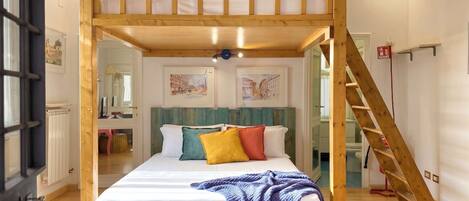 Une chambre avec un lit superposé, une échelle en bois, une salle de bain avec douche et vue sur la rue.