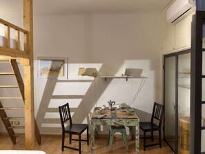 A room with a wooden ladder, a dining table with chairs, a small shelf with items, and a door with a glass panel. - Loft del Cefalo - In the heart of the old town (Roma)