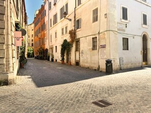 Eine Kopfsteinpflasterstraße mit Gebäuden an beiden Seiten, einer Mülltonne und einem Schild für die Tim Van Laere Gallery Rom.