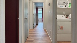 A hallway with wooden flooring, white walls, and a laundry area with a washing machine and dryer.