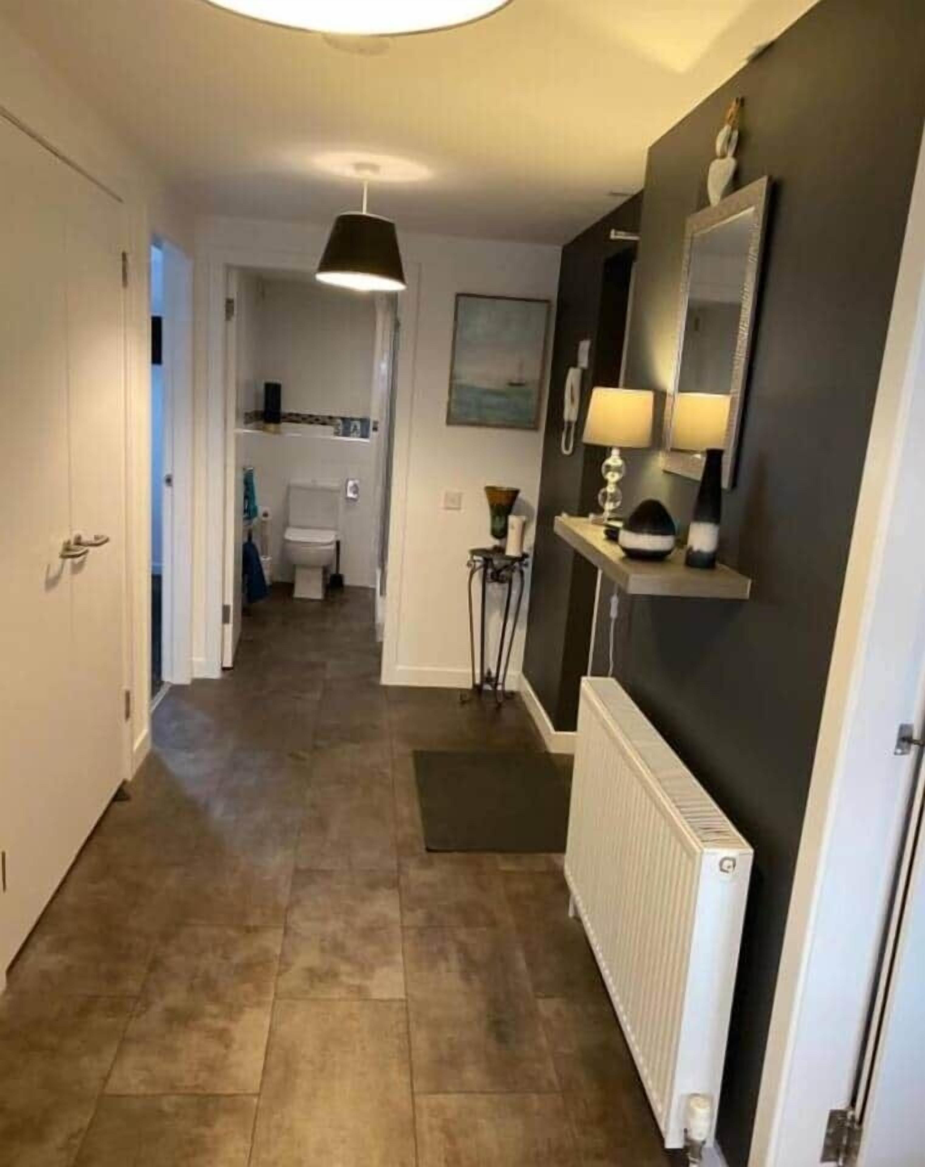 En hall med ett element, en dörr, en lampa och en spegel på väggen.