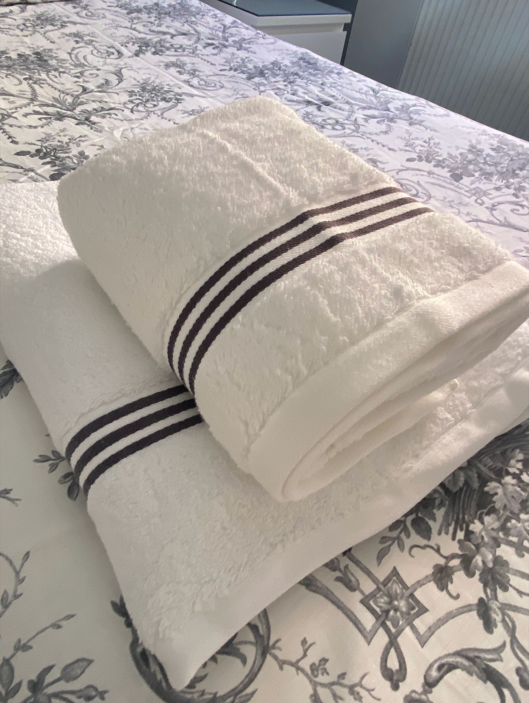 Twee opgevouwen handdoeken met donkere strepen op een bed met een bloemenprint bedspread.