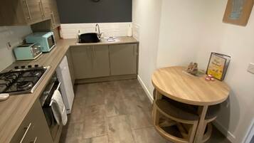 A compact kitchen with a gas stove, a sink, and a microwave. There's a round wooden table with chairs and a clock on the wall.