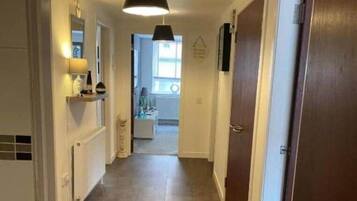 A narrow hallway with a black pendant light, white walls, and a tiled floor.