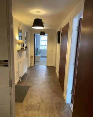 Um corredor estreito com uma luminária pendente preta, paredes brancas e chão de azulejos.