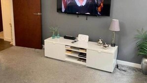 Olohuoneessa on seinälle asennettu televisio, valkoinen mediakeskus ja ovi.