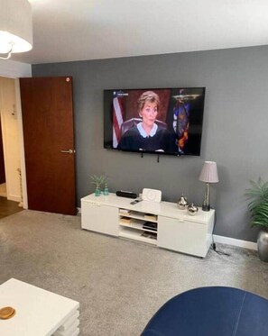 Uma sala de estar com televisão na parede, um rack branco e uma porta.