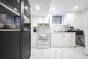 A modern kitchen with white cabinets, a stove, and a microwave. - Bright Basement Suite w Parking Near Mclennan Park (Kitchener)