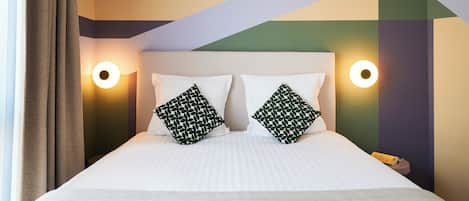 A bed with white bedding, two pillows with a leaf pattern, and two wall-mounted lights.