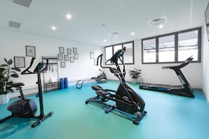 A gym with various exercise equipment, including treadmills and an elliptical machine, on a blue floor with white walls and framed pictures. - Ibis Styles Aix-En-Provence Université (Aix-en-Provence)