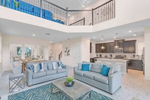 A spacious living area with two sofas, a coffee table, and a dining area with a large window. - 5BD Paradise Retreat Champions Gate W/Xbox & VR (Kissimmee)