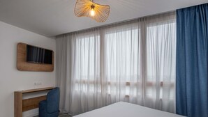 Een moderne hotelkamer met een groot bed, een bureau, een stoel, een televisie en dunne gordijnen.