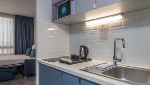 Een kleine keuken met een magnetron, waterkoker en spoelbak.