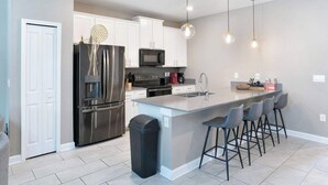 A modern kitchen with stainless steel appliances, a central island with bar stools, and pendant lighting. - ChampionsGate 5BR | Pool, Xbox + Oasis Resort (Davenport)