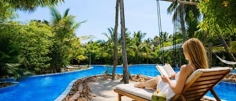 A poolside area with a lounge chair, a wooden swing, and a table with a coconut.