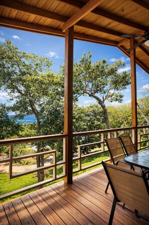 Eine Holzterrasse mit Tisch und Stühlen mit Blick auf eine üppige Landschaft mit Bäumen und blauem Himmel.